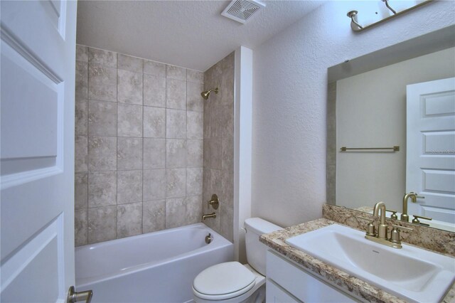 full bathroom featuring a textured ceiling, toilet, tiled shower / bath, and vanity