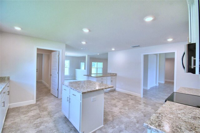 kitchen with white cabinets, a center island, and light stone countertops