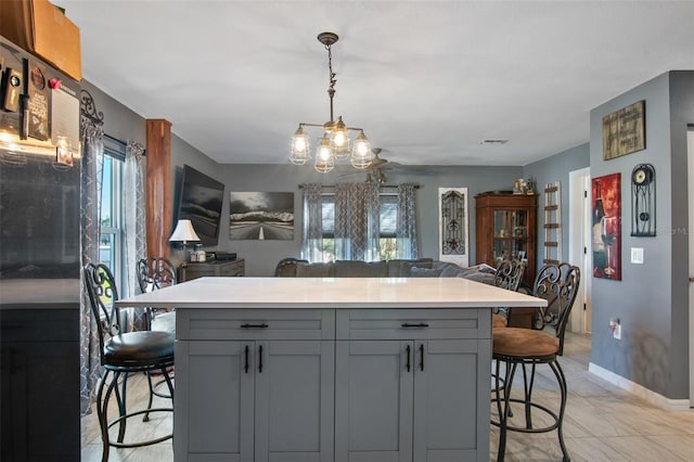 kitchen with light tile floors, gray cabinets, hanging light fixtures, a breakfast bar area, and an inviting chandelier