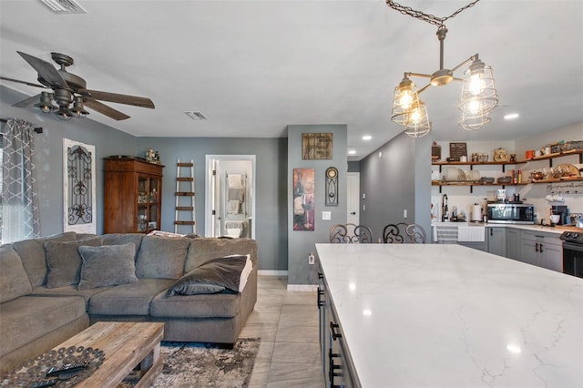 kitchen with light tile floors, gray cabinetry, ceiling fan with notable chandelier, and pendant lighting