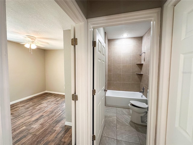 bathroom with tiled shower / bath combo, toilet, ceiling fan, hardwood / wood-style floors, and a textured ceiling