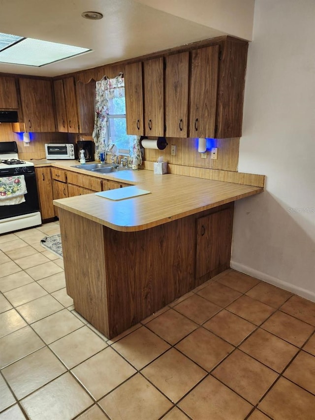 kitchen featuring light tile patterned floors, a peninsula, white gas range, light countertops, and under cabinet range hood