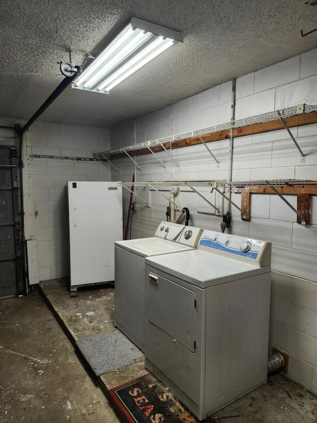 clothes washing area featuring concrete block wall, a textured ceiling, a garage, laundry area, and independent washer and dryer