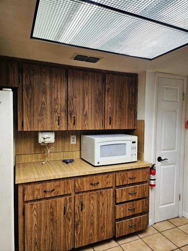 kitchen with light tile patterned floors, white appliances, visible vents, light countertops, and brown cabinets