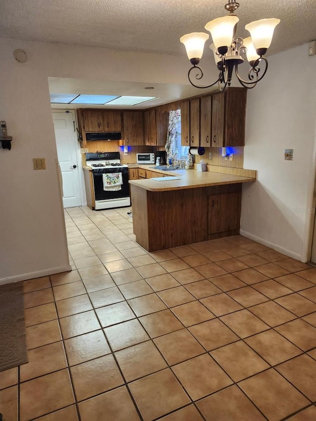 kitchen featuring under cabinet range hood, a peninsula, a sink, light countertops, and white gas range