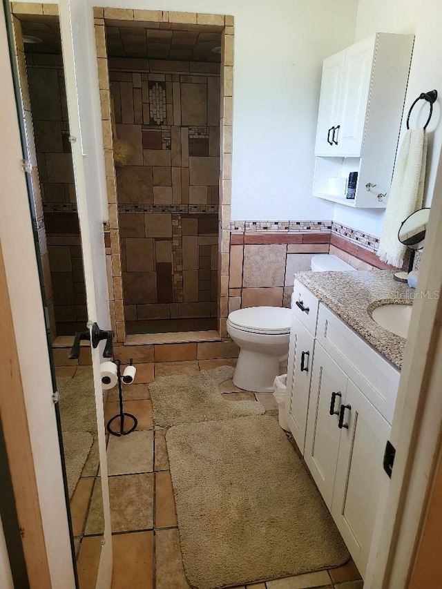 bathroom featuring tiled shower, toilet, tile patterned floors, vanity, and tile walls