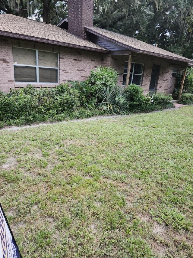 view of home's exterior with brick siding, a chimney, and a lawn