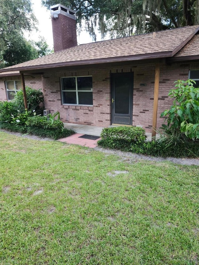 exterior space featuring a shingled roof, a front yard, brick siding, and a chimney