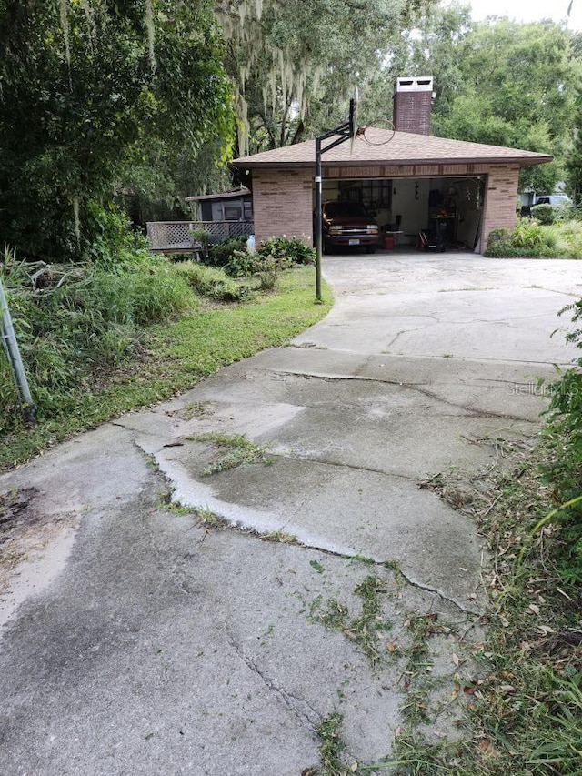 view of side of property with a garage, brick siding, driveway, and a chimney