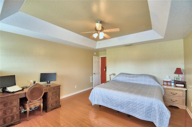 bedroom featuring a textured ceiling, a raised ceiling, ceiling fan, and light hardwood / wood-style flooring