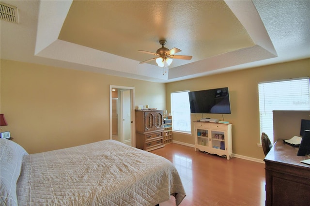 bedroom with ceiling fan, a raised ceiling, hardwood / wood-style floors, and a textured ceiling