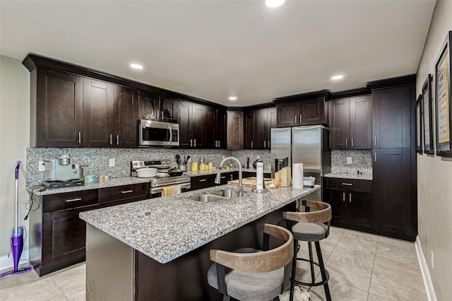kitchen featuring backsplash, appliances with stainless steel finishes, sink, light stone countertops, and a breakfast bar area