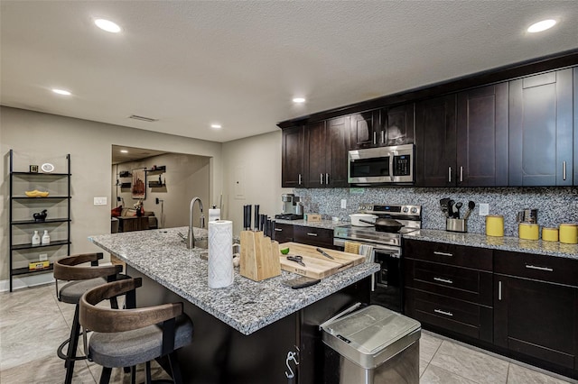 kitchen with a kitchen bar, appliances with stainless steel finishes, tasteful backsplash, and light stone countertops