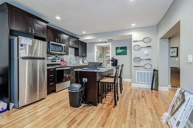 kitchen with a breakfast bar area, light hardwood / wood-style flooring, appliances with stainless steel finishes, and dark brown cabinets