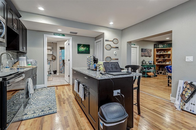 kitchen with light stone counters, tasteful backsplash, a kitchen bar, stainless steel appliances, and light wood-type flooring