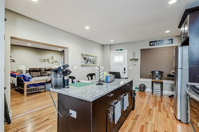 kitchen featuring dark brown cabinets, light stone counters, stainless steel appliances, and light wood-type flooring