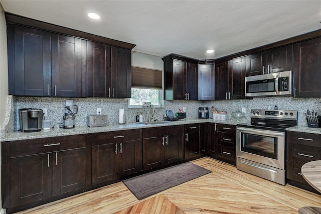 kitchen featuring light stone counters, tasteful backsplash, dark brown cabinets, stainless steel appliances, and sink