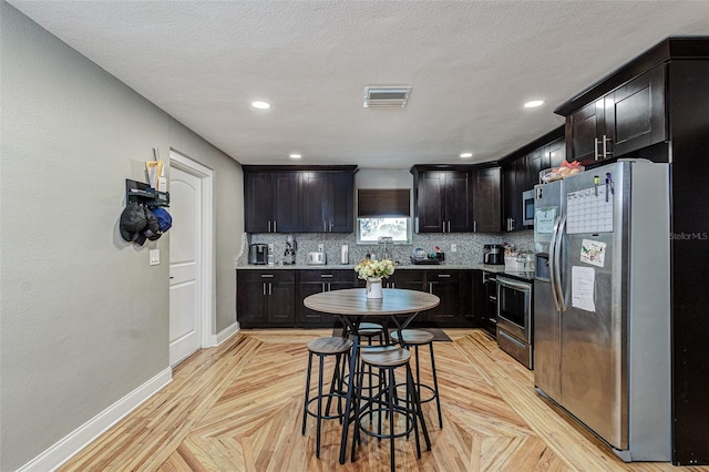 kitchen with light parquet flooring, stainless steel appliances, a kitchen bar, and a textured ceiling