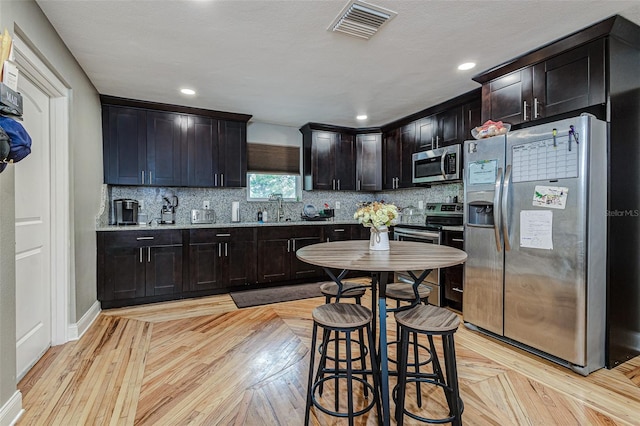 kitchen featuring a breakfast bar, appliances with stainless steel finishes, backsplash, sink, and light parquet flooring