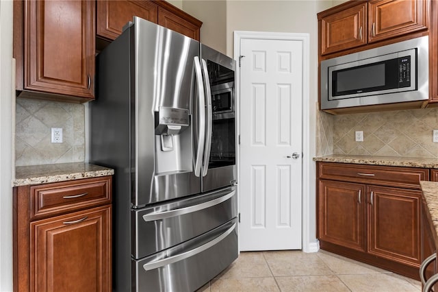 kitchen with tasteful backsplash, appliances with stainless steel finishes, light tile floors, and light stone counters