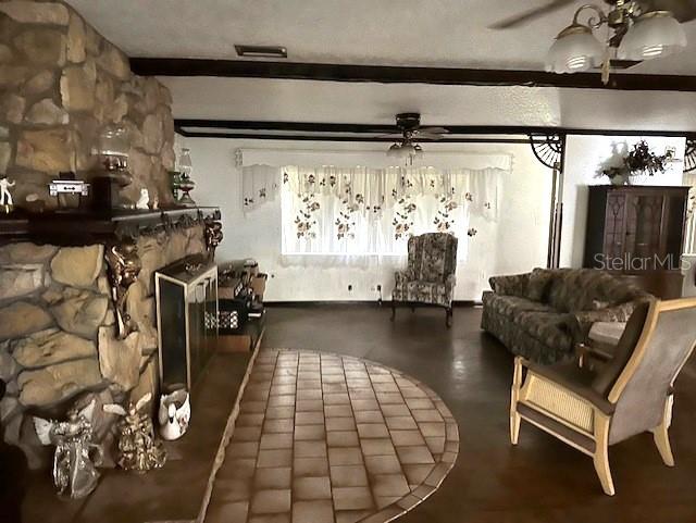 living room with ceiling fan, beam ceiling, and a stone fireplace