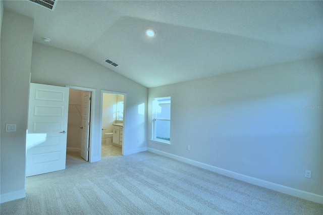 unfurnished bedroom with connected bathroom, a walk in closet, light carpet, a closet, and lofted ceiling