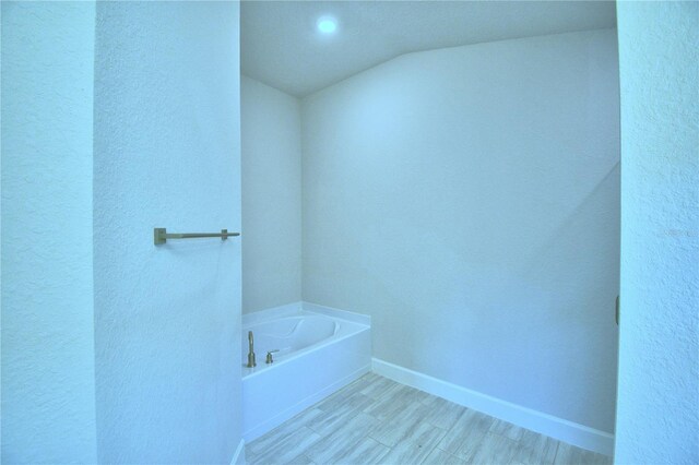 bathroom with a tub, hardwood / wood-style floors, and vaulted ceiling