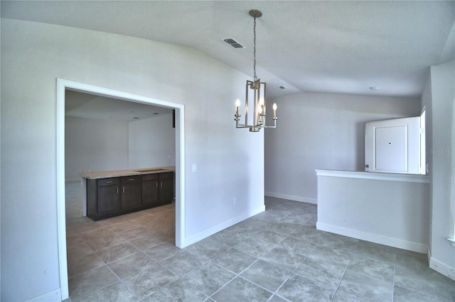 tiled spare room featuring a chandelier and vaulted ceiling