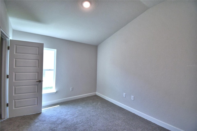 spare room with a textured ceiling, lofted ceiling, and dark colored carpet