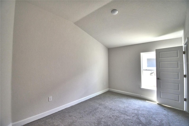 spare room with a textured ceiling, dark carpet, and lofted ceiling