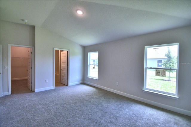 unfurnished bedroom with carpet, a spacious closet, lofted ceiling, and multiple windows