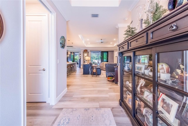 hall with a raised ceiling, crown molding, and light hardwood / wood-style flooring