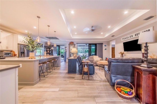 living room with a raised ceiling, ceiling fan, and crown molding