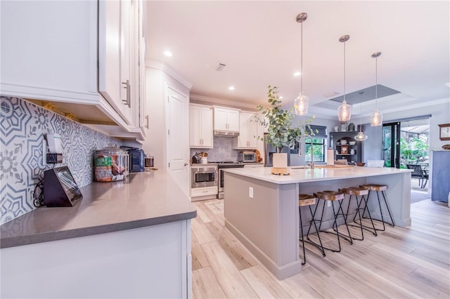 kitchen with pendant lighting, a raised ceiling, a kitchen breakfast bar, white cabinets, and light wood-type flooring