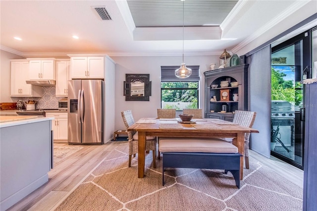 dining space featuring crown molding, a tray ceiling, and light hardwood / wood-style flooring