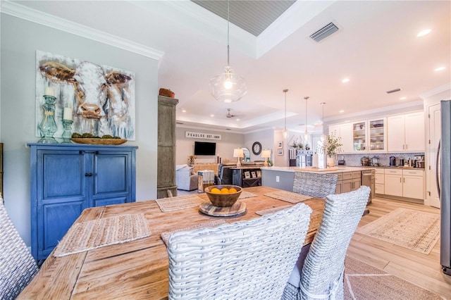 dining room featuring crown molding, a tray ceiling, and light wood-type flooring