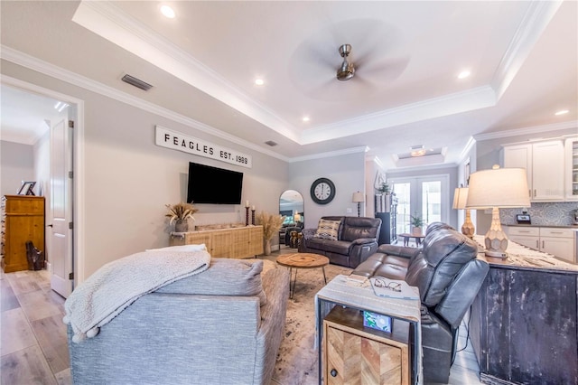 living room with a tray ceiling, ornamental molding, light hardwood / wood-style flooring, and french doors