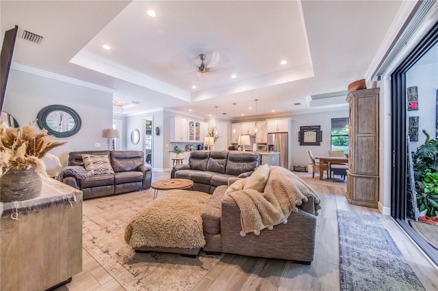 living room with a raised ceiling, ornamental molding, and light wood-type flooring