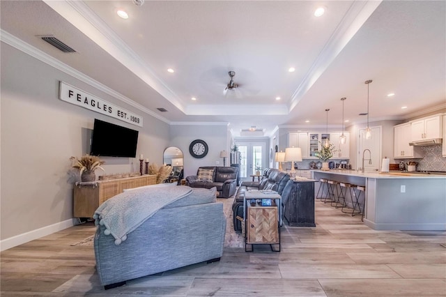 living room featuring ornamental molding, a tray ceiling, and light hardwood / wood-style flooring