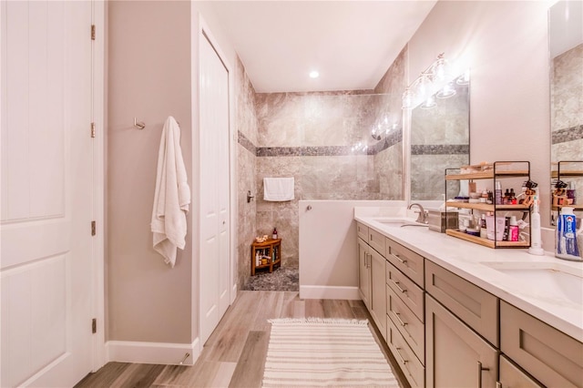 bathroom with double vanity, a tile shower, and wood-type flooring