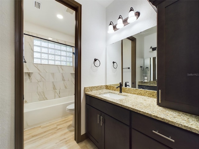 full bathroom with hardwood / wood-style floors, toilet, tiled shower / bath combo, and vanity