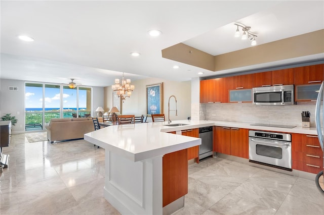 kitchen featuring kitchen peninsula, sink, stainless steel appliances, tasteful backsplash, and ceiling fan with notable chandelier