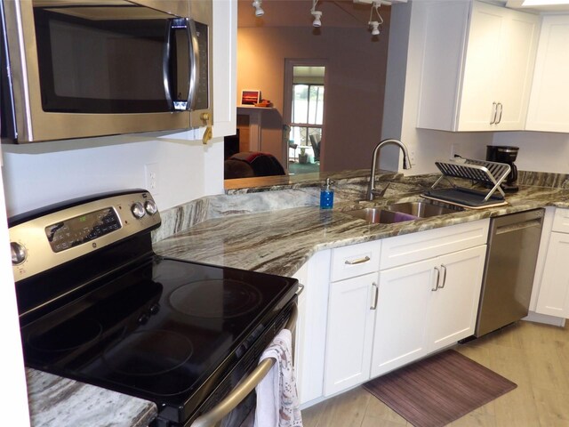 kitchen featuring sink, appliances with stainless steel finishes, light stone counters, light hardwood / wood-style floors, and white cabinets