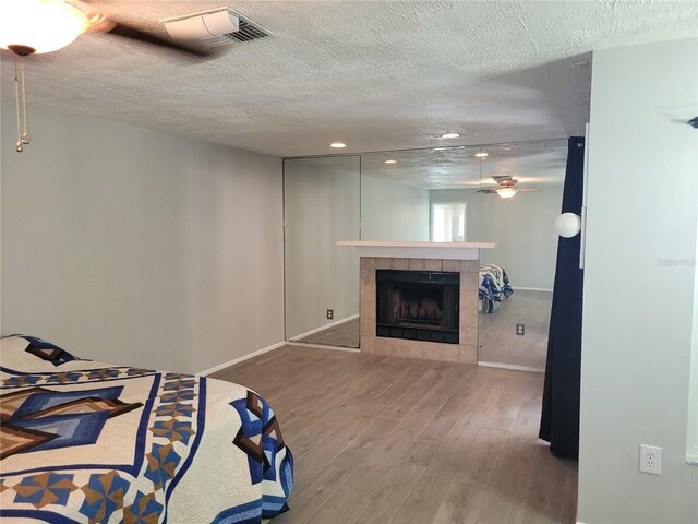 bedroom with a tiled fireplace, wood-type flooring, and a textured ceiling