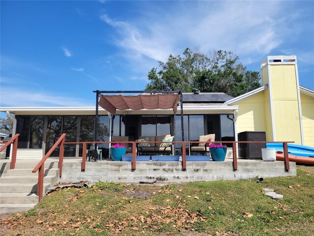 rear view of property featuring a patio area, a sunroom, and solar panels