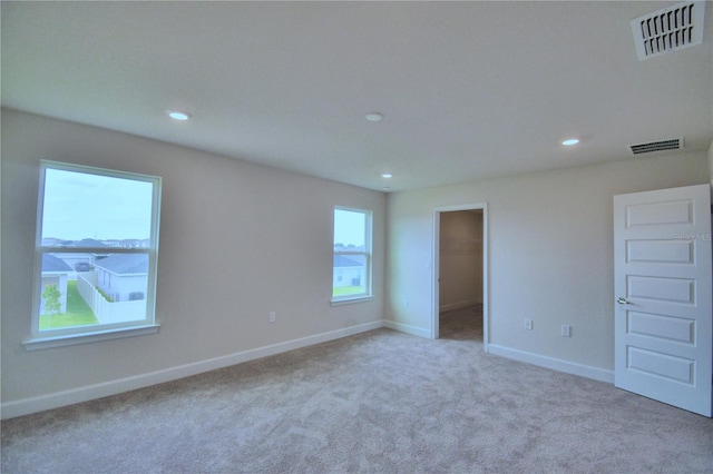 unfurnished bedroom with light colored carpet, a spacious closet, a closet, and multiple windows