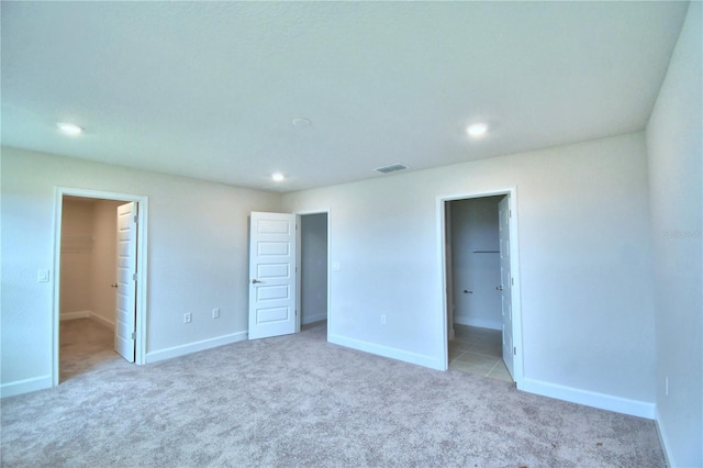 unfurnished bedroom featuring light carpet, connected bathroom, a walk in closet, and a closet