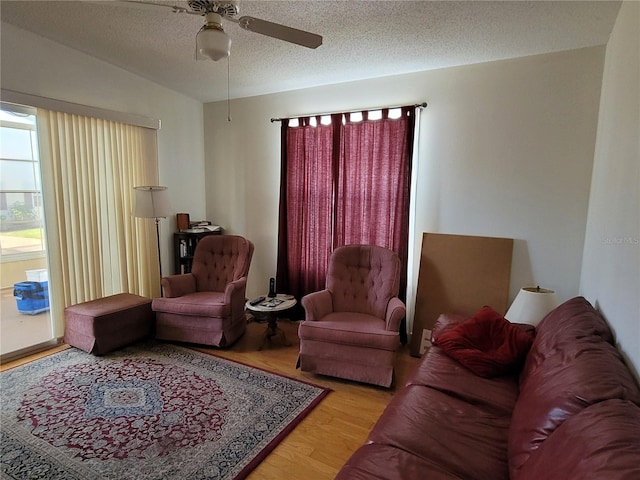 living room with ceiling fan, light wood-type flooring, and a textured ceiling