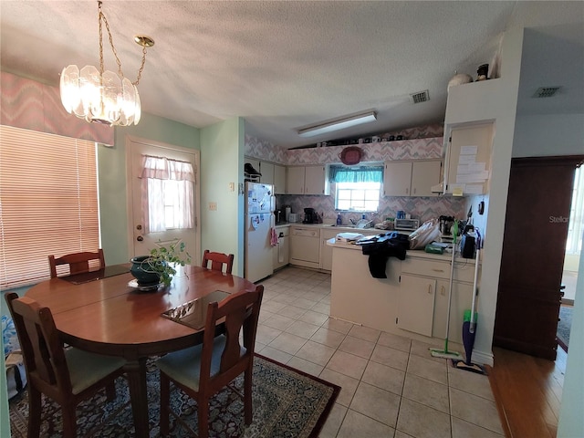 dining room with light tile flooring, lofted ceiling, a textured ceiling, sink, and a chandelier