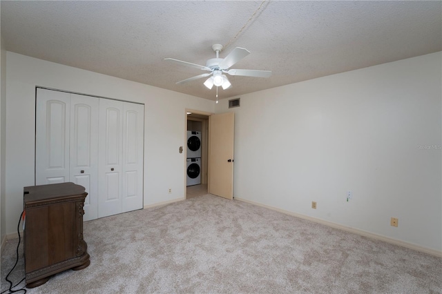 unfurnished bedroom featuring light colored carpet, ceiling fan, a textured ceiling, a closet, and stacked washer and clothes dryer